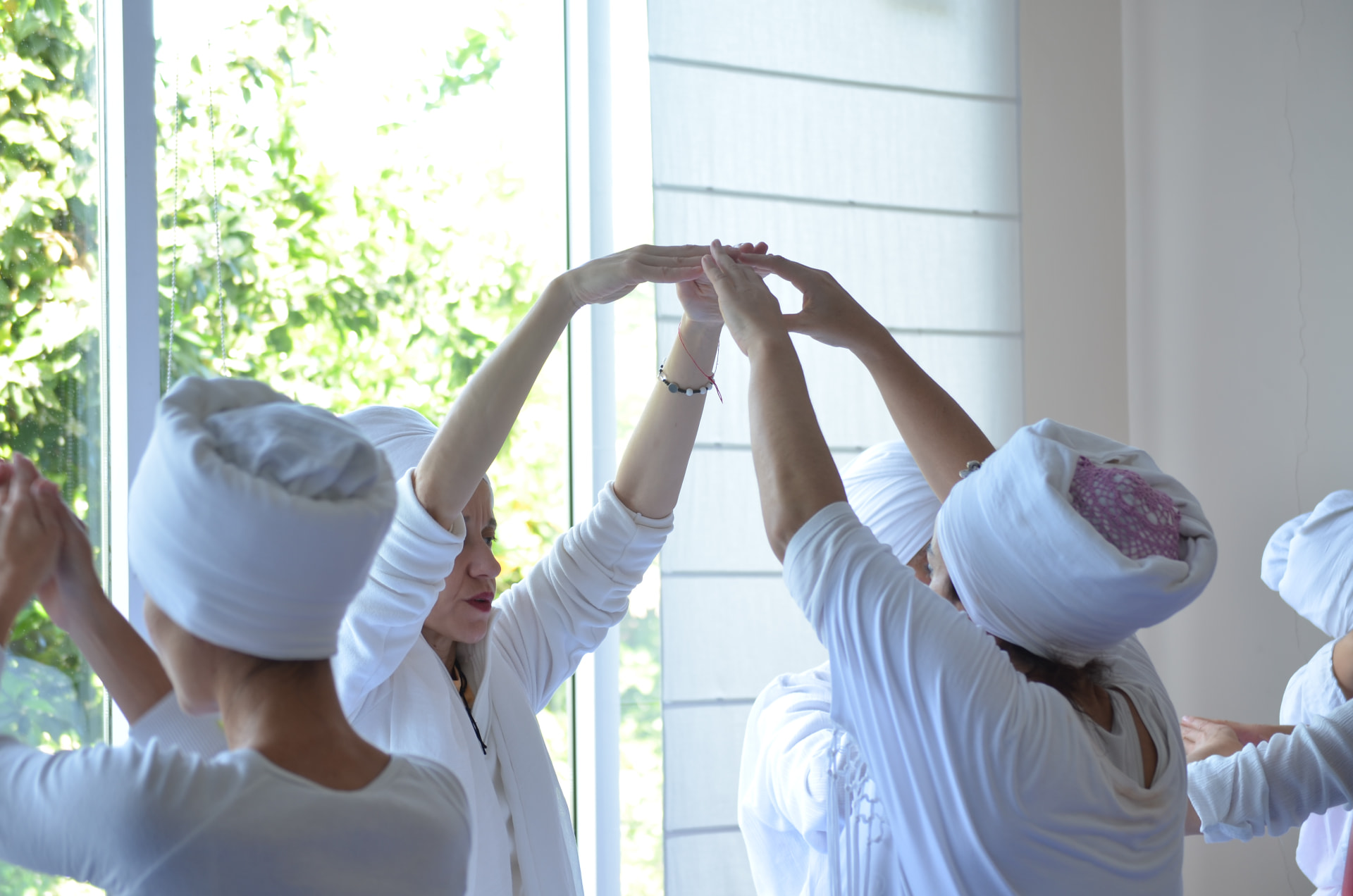 Grupo practicando Kundalini Yoga con los brazos en alto frente a una ventana luminosa